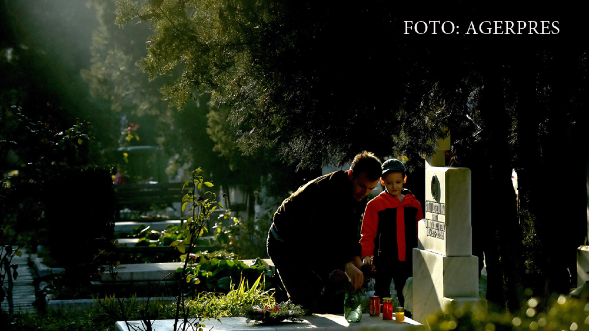 Un barbat insotit de un copil aprind lumanari la un mormant din Cimitirul Eroii Revolutiei.