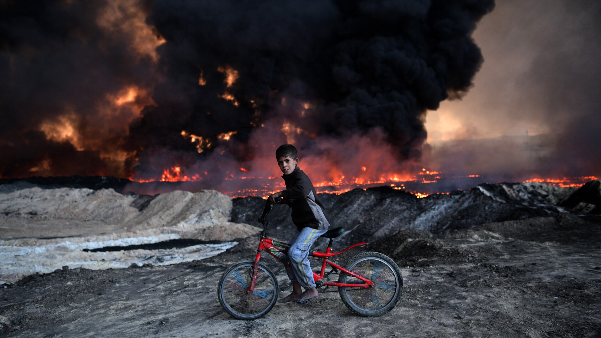 Un baiat pe bicicleta se opreste langa un camp petrolier incendiat de ISIS, in Mosul