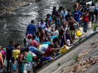 Venezuelenii adună apă dintr-un canal. Pana masivă de curent se prelungește