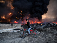 Un baiat pe bicicleta se opreste langa un camp petrolier incendiat de ISIS, in Mosul
