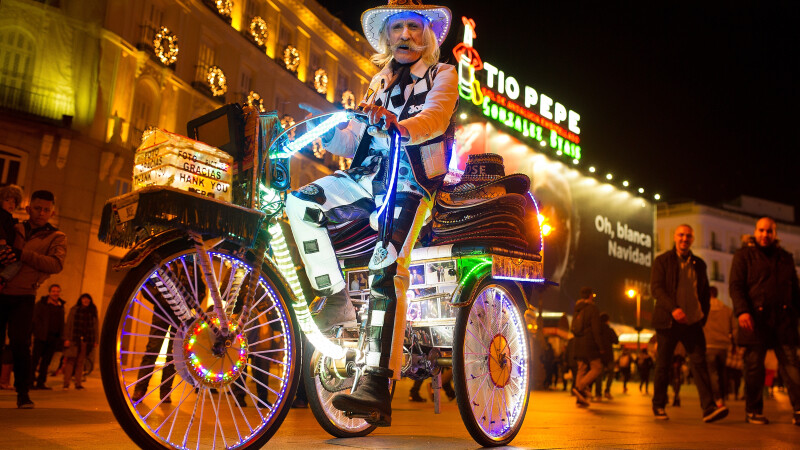 Un artist stradal merge cu bicicleta sa luminata, in Madrid, inaintea deschiderii targului de Craciun