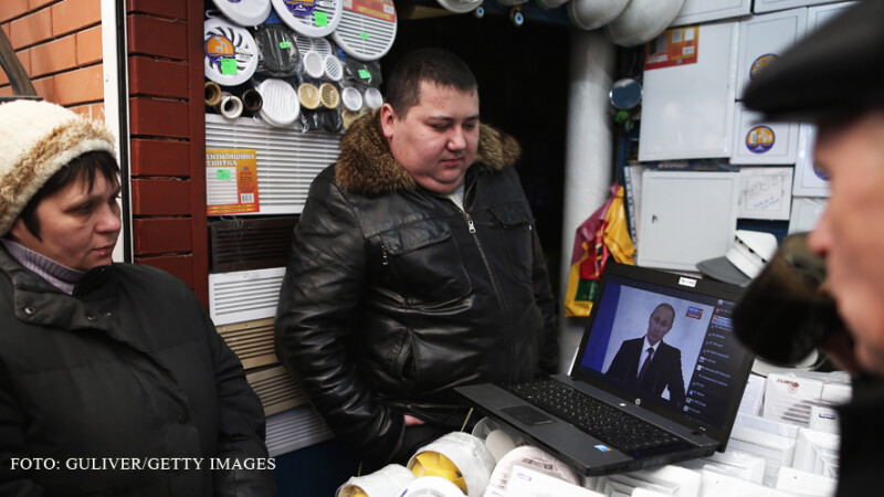 rusi se uita in piata la un laptop cu Putin