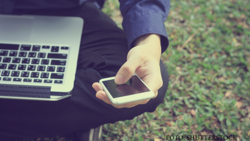 barbat care sta pe iarba cu un laptop si un telefon