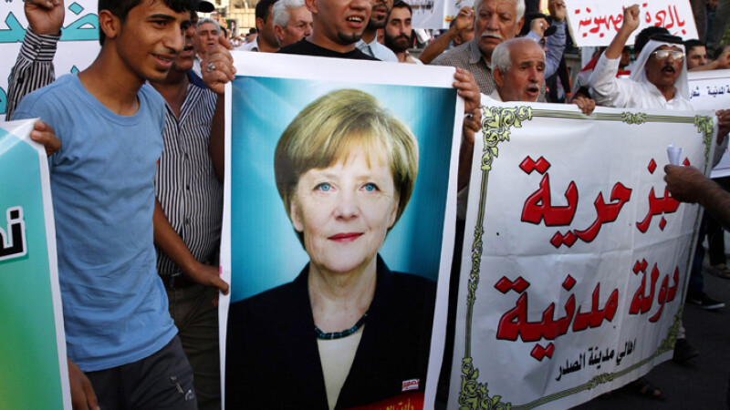 refugiati purtand o pancarta cu portretul lui Merkel